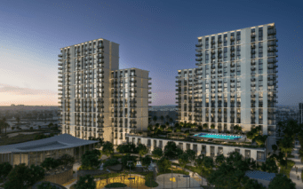Une vue nocturne du complexe d'appartements Hillsedge révèle deux hauts bâtiments ornés de nombreux balcons. Ils entourent une cour centrale présentant une piscine éclairée et des jardins bien entretenus, tandis que le ciel passe élégamment du crépuscule à l'obscurité.