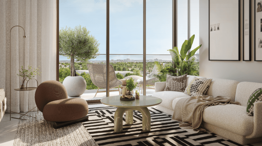 Le salon moderne comprend une chaise marron moelleuse, un canapé blanc et une table basse en verre sur un tapis géométrique noir et blanc. De grandes fenêtres s'ouvrent sur le balcon Hillsedge, orné de chaises, de plantes et d'une vue imprenable sur la verdure lointaine et le paysage urbain.