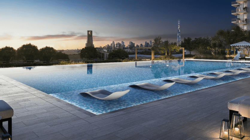 Une piscine à débordement sur le toit avec des chaises longues immergées à Hillsedge surplombe l'horizon de la ville au crépuscule. Le ciel est un mélange de tons chauds, tandis que les gratte-ciel de la ville sont faiblement éclairés au loin. La zone est entourée d'une végétation luxuriante et d'un éclairage décoratif.