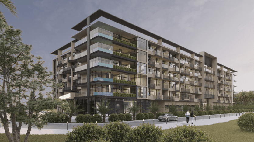 Un immeuble moderne de six étages avec des balcons en verre et de la verdure. Une personne marche sur le chemin et une voiture est garée à proximité. La scène se déroule sous un ciel nuageux et est entourée d'arbres et de buissons.