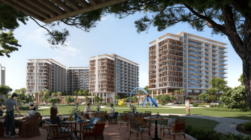 Les gens sont assis sur une terrasse avec des tables au premier plan, profitant d'une vue sur le paysage verdoyant et luxuriant de Parkfive et ses arbres imposants. Des immeubles modernes de grande hauteur et une aire de jeux colorée peuvent être vus en arrière-plan sous un ciel bleu clair.