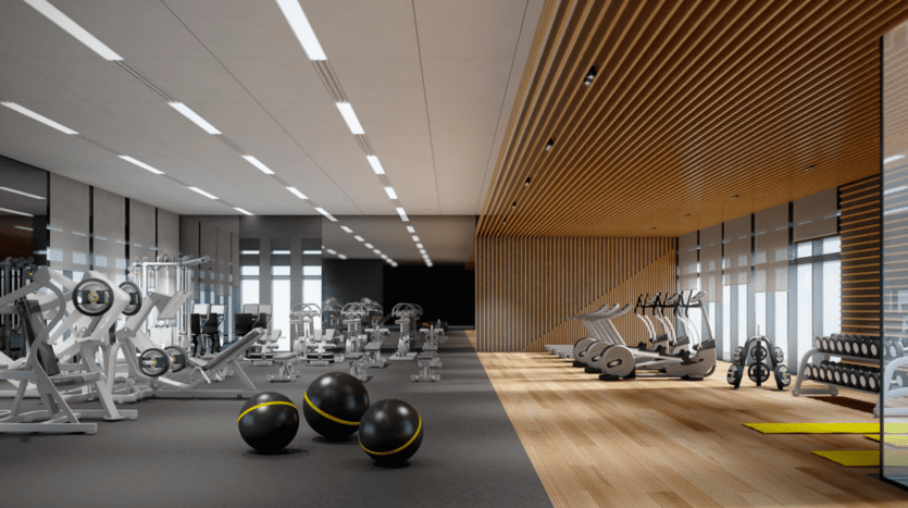 Parkfive propose une salle de sport moderne avec des équipements d'exercice, notamment des tapis de course, des appareils de musculation et des ballons d'exercice. La salle est dotée d'un mélange de parquet et de revêtement de sol en caoutchouc, avec une abondante lumière naturelle qui pénètre à travers de grandes fenêtres sur un côté.