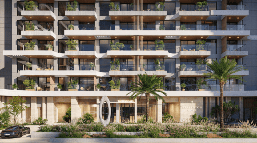 L'immeuble moderne Ellington Cove se dresse sur plusieurs étages et balcons ornés de plantes luxuriantes. Son entrée est marquée par une sculpture ovale distinctive et d'élégants palmiers, tandis qu'une voiture est commodément garée devant.