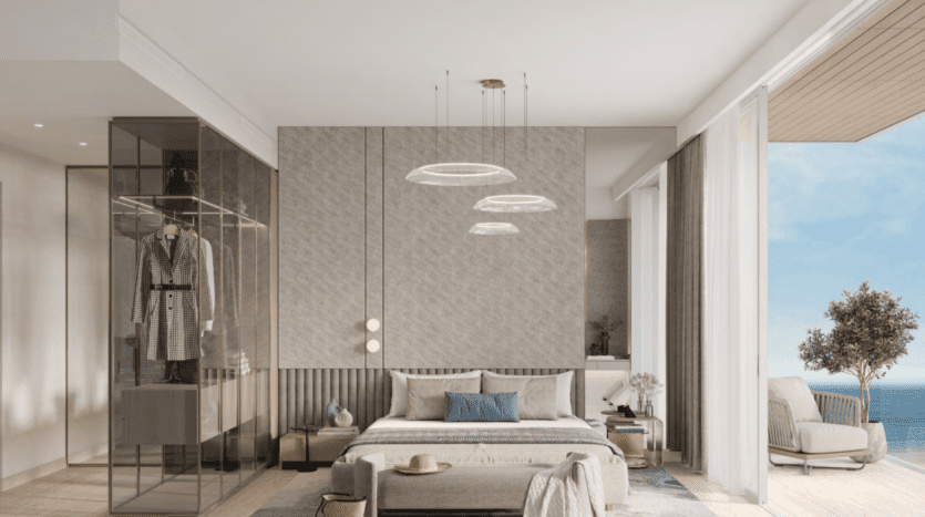 Chambre moderne avec un grand lit, une armoire en verre et un coin salon. Des suspensions sont suspendues au plafond. Une porte coulissante s'ouvre sur un balcon avec vue sur l'océan d'Ellington Cove. Les tons terreux et la décoration minimaliste créent une atmosphère sereine.