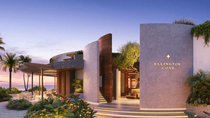 Ellington Cove est un bâtiment moderne en bord de mer avec une architecture élégante et incurvée et une végétation luxuriante. Un panneau affiche fièrement son nom tandis que l'océan et les palmiers se balancent en arrière-plan sous un ciel de coucher de soleil vibrant.