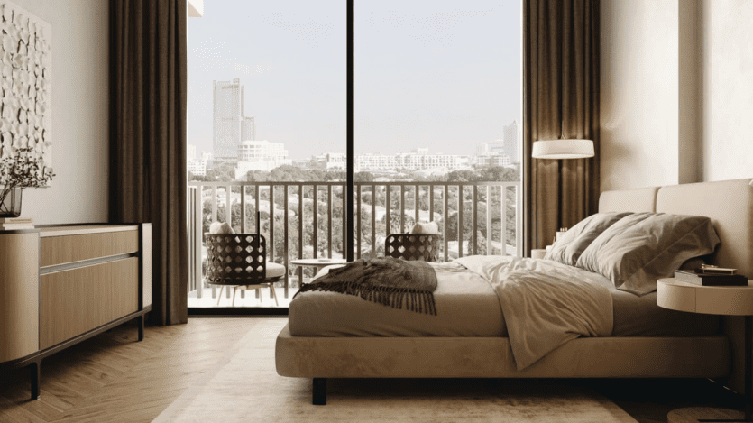 Une chambre moderne avec une grande fenêtre donnant sur un paysage urbain respire le style Arisha. La chambre dispose d'un lit beige, d'une commode en bois et de tables de chevet. Deux chaises sont situées sur la terrasse extérieure, avec de la verdure visible au-delà. Les tons neutres créent une ambiance chaleureuse.