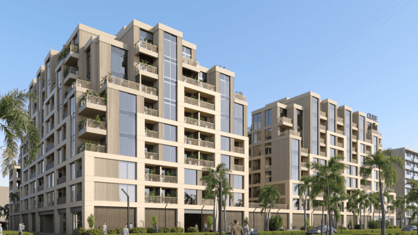 Arisha Terraces, un complexe d'appartements moderne à plusieurs étages, dispose de grandes fenêtres, de balcons et de palmiers bordant la rue. Le bâtiment présente un mélange de matériaux clairs et foncés avec un panneau indiquant « Olive » sur la façade sur un fond de ciel bleu clair.