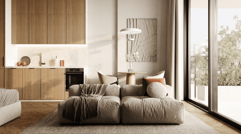 Le salon moderne de l'Arisha Terraces comprend un canapé beige avec des coussins ronds et un plaid texturé. Des armoires en bois bordent un mur, avec un plan de travail et des appareils intégrés. Une petite table à manger se trouve à proximité, tandis que de grandes fenêtres offrent une vue imprenable sur la verdure extérieure.