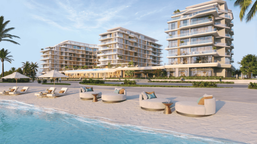 Vue en front de mer d'appartements de luxe modernes aux façades vitrées, entourés de palmiers. La plage de sable au premier plan est dotée de chaises longues et de tables rondes, avec un ciel bleu clair au-dessus.