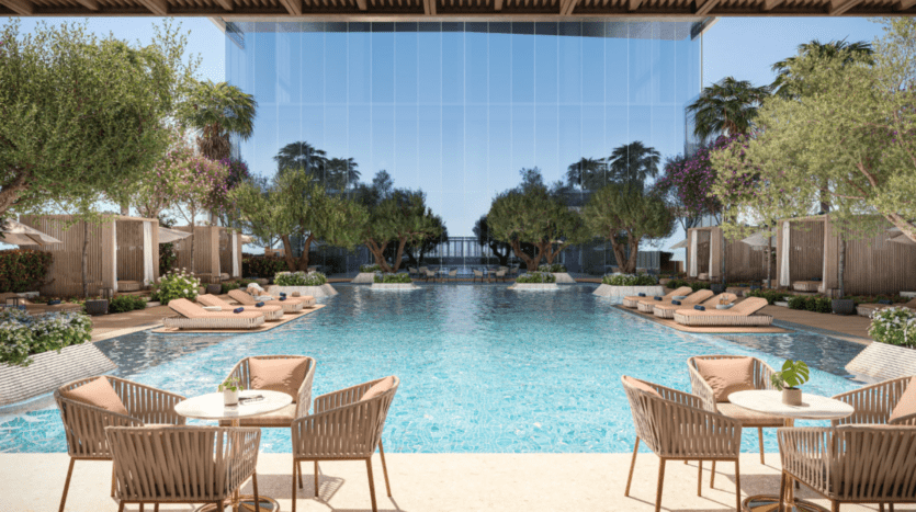 La luxueuse piscine extérieure du Mr C Downtown propose des chaises longues entourées d'une végétation luxuriante et de cabanes modernes. Un bâtiment en verre réfléchissant en arrière-plan renforce l'ambiance sereine. Des tables avec des chaises au premier plan créent une atmosphère relaxante dans cet élégant cadre hôtelier du centre-ville.