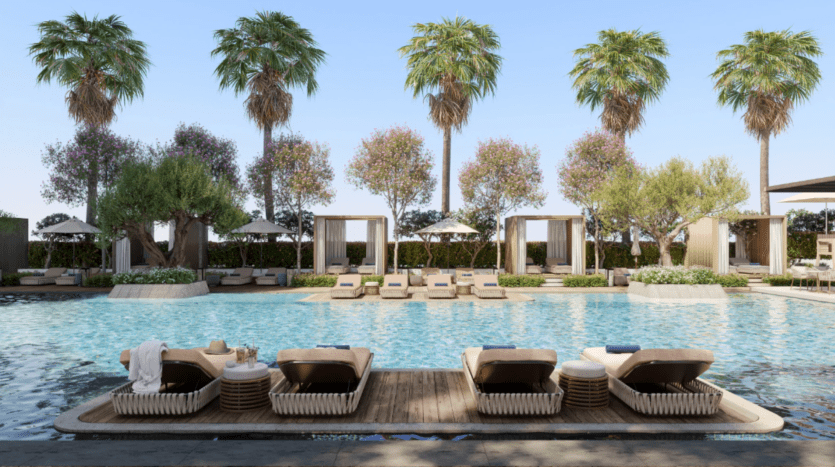 Piscine extérieure luxueuse du centre-ville de Mr C avec chaises longues et cabanons, entourée de palmiers et de plantes à fleurs. Des serviettes et un chapeau reposent sur les chaises longues, tandis que le ciel reste clair et bleu.