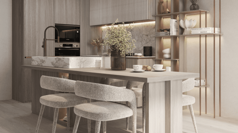 Cuisine moderne sur Cove Boulevard avec des meubles en bois clair et un îlot en marbre avec un vase de fleurs. Trois chaises rembourrées sont placées contre l'îlot. Des étagères ouvertes avec des objets de décoration et des appareils intégrés complètent le design élégant.