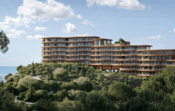 Situé à flanc de colline, cet hôtel moderne de Dubaï présente une architecture élégante en panneaux de verre et de bois, entouré d'une végétation luxuriante. Surplombant la paisible baie d'Asora, il offre une vue imprenable sur l'océan sous un ciel partiellement nuageux.