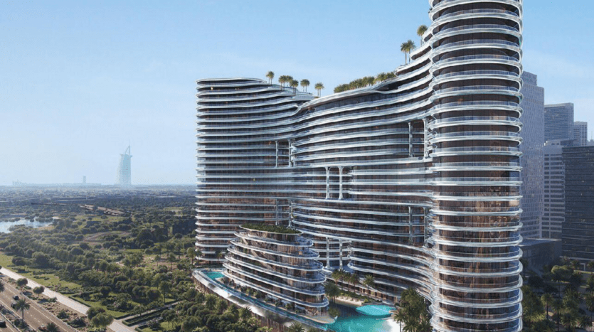 Un gratte-ciel moderne et incurvé, Binghatti Aquarise, avec des façades en verre et des toits verts, se dresse à côté d'une piscine, entouré d'un paysage luxuriant, avec une tour emblématique lointaine visible contre le ciel bleu.
