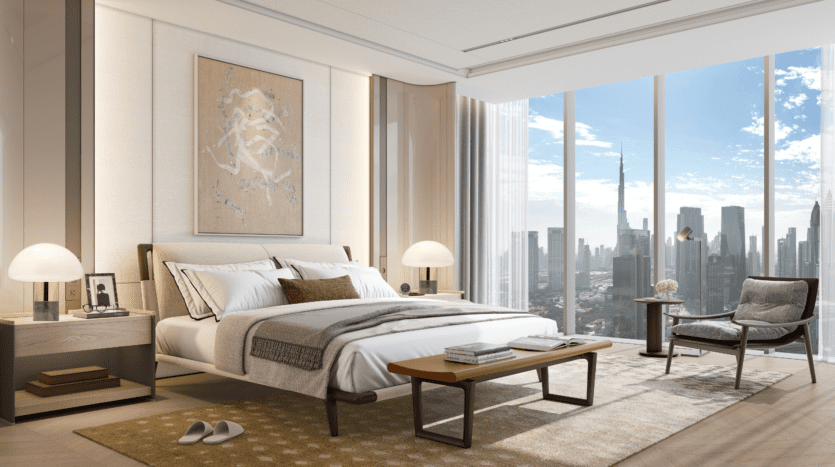 Modern room with large picture windows overlooking the city's rooftops, featuring a carefully made bed, bedside tables with lamps, a comfortable chair, coffee table, rug and abstract wall art above the bed.