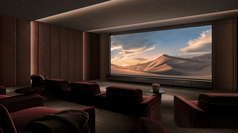A modern home cinema with red reclining seats faces a large screen showing a picturesque desert landscape at sunset. The ceiling is lit up like stars, and a popcorn bucket sits on a side table.