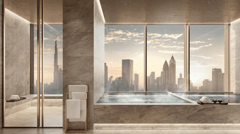 Luxurious marble bathroom with large bathtub next to picture windows offering breathtaking views of the city at sunset. A towel rack and rolled towels are visible next to the bathtub.