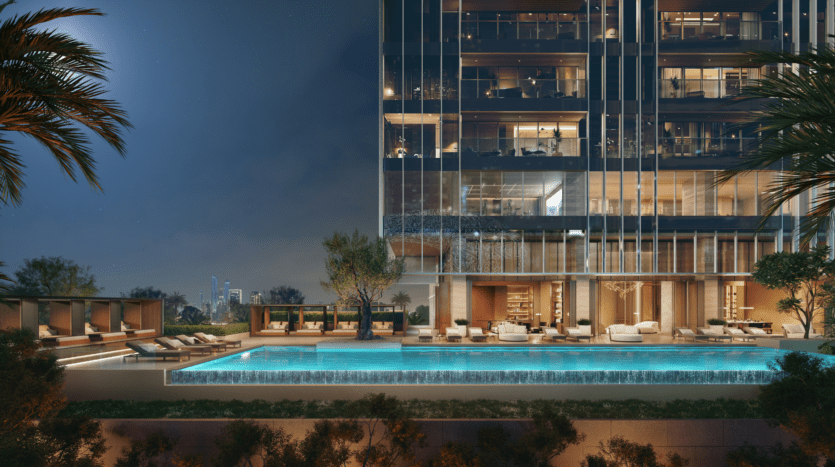 A modern luxury apartment building at night features a well-lit pool, poolside loungers, palm trees and elegant outdoor seating, with city lights visible in the background.