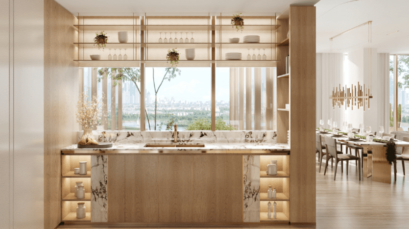 Cuisine moderne avec armoires en bois clair, comptoirs en marbre, étagères ouvertes avec plantes et plats, une grande fenêtre donnant sur l'île de Wynwood Dubaï et une salle à manger adjacente avec une table élégante et un lustre.