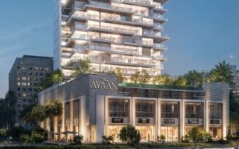 Ayaan Heights 1 by IGO est un immeuble moderne de plusieurs étages baptisé "Ayaan", qui propose des magasins aux étages inférieurs et une tour au-dessus avec des balcons et de la verdure, magnifiquement illuminée le soir.