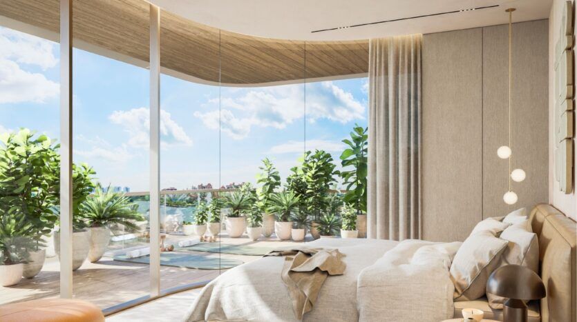 Une chambre moderne à l'Avida Residences Dubai Islands avec des fenêtres en verre allant du sol au plafond et donnant sur un balcon rempli de plantes en pot. La chambre se caractérise par un lit bien fait, des tons neutres, la lumière naturelle du soleil et une décoration minimaliste.