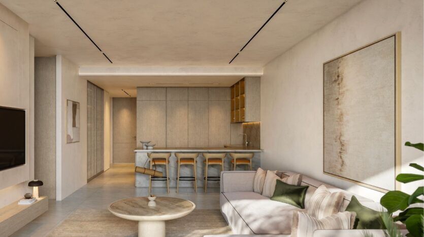 Salon et cuisine modernes à l'Avida Residences Dubai Islands avec des tons neutres, un canapé beige, des coussins verts, une table basse ronde, des tabourets de bar sur un îlot en marbre, un grand tableau mural abstrait et un décor minimaliste, bien éclairé par des lumières naturelles et encastrées.