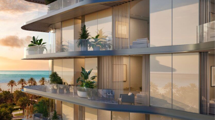 Avida Residences Dubai Islands propose des appartements de luxe modernes dotés de grands balcons en verre, de plantes en pot et de sièges extérieurs donnant sur les palmiers et l'océan au coucher du soleil, créant ainsi une atmosphère sereine et élégante.