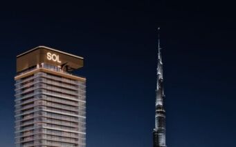 Une tour moderne, la Sol Luxe Tower, est illuminée la nuit et se dresse à côté de la Burj Khalifa, plus haute et semblable à une aiguille, dans un ciel sombre.