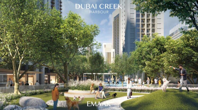 Des personnes et des chiens profitent d'un parc verdoyant entouré de grands immeubles modernes dans le Dubai Creek Harbour, près de la Résidence Lyvia by Palace. Des arbres, des allées et des bancs créent un espace extérieur urbain et animé, avec les logos d'EMAAR et de Dubai Creek Harbour visibles.