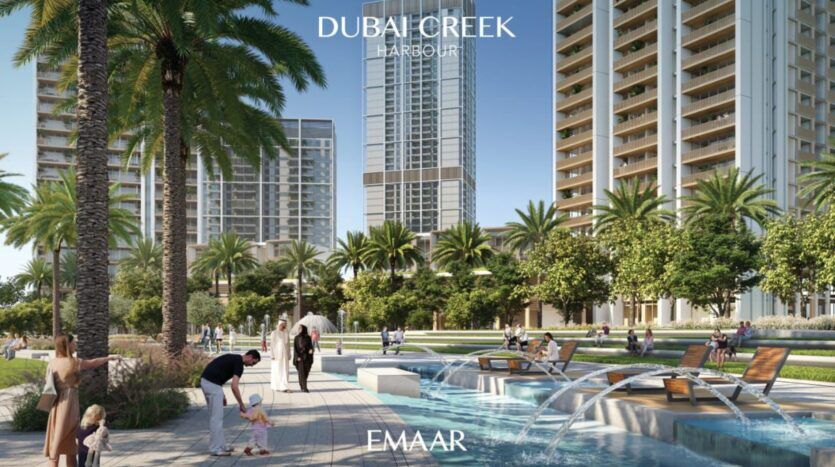 Des gratte-ciel modernes et des palmiers entourent un parc paysager avec une fontaine, des chaises longues et des gens qui se détendent dans le port de Dubai Creek, près de la Résidence Lyvia by Palace. Un homme aide un enfant au bord de l'eau tandis que d'autres profitent de la journée ensoleillée.