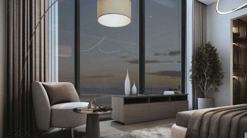Une chambre à coucher SkyParks moderne aux tons gris et beiges comprend une chaise confortable, une petite table d'appoint, une grande fenêtre avec vue sur le coucher de soleil, un lampadaire, des vases décoratifs et une plante en pot à côté d'un lit avec une couverture neutre.