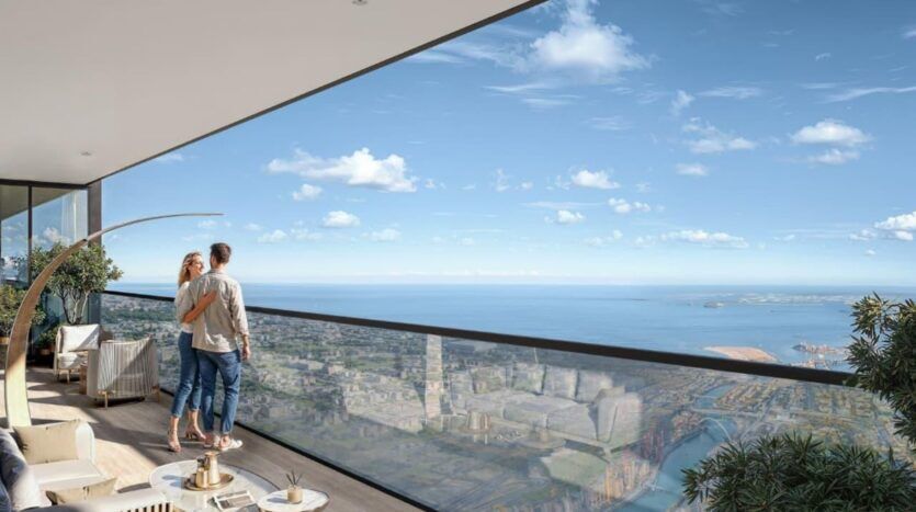 Un couple se tient sur un balcon moderne de SkyParks qui surplombe un paysage urbain et un vaste océan sous un ciel bleu clair, entouré d'un mobilier d'extérieur élégant et de plantes vertes.