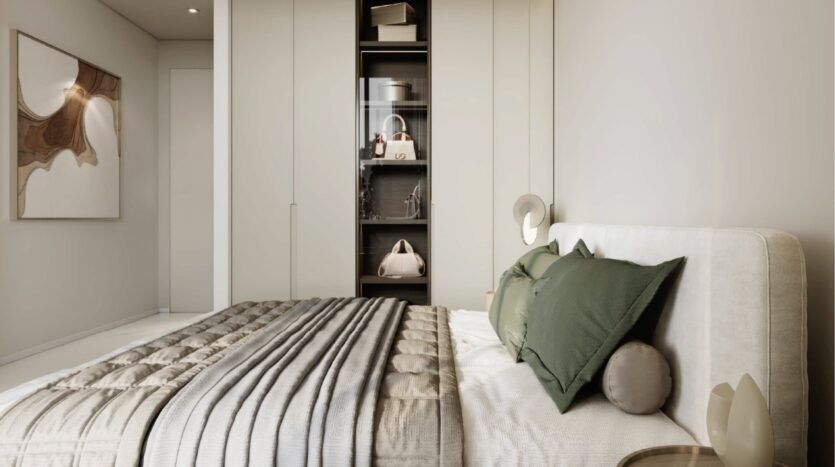 Une chambre à coucher moderne avec un lit soigneusement fait avec des oreillers verts et gris, une tête de lit rembourrée et une couette à rayures grises. Des placards encastrés et des étagères contenant des sacs et des objets de décoration évoquent le luxe de Franck Muller Yachting à Dubai Maritime City. Des œuvres d'art abstraites ornent le mur.
