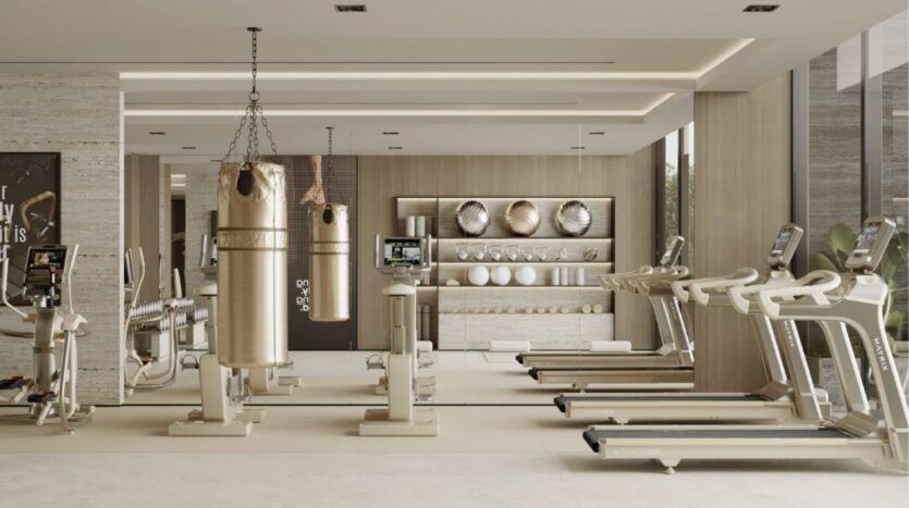 Salle de sport moderne aux tons beiges, équipée de tapis de course, de vélos d'appartement, de sacs de frappe, d'étagères à poids et d'appareils fixés au mur. Inspiré par le Franck Muller Yachting à Dubai Maritime City, l'espace est bien éclairé par de grandes fenêtres et un décor minimaliste.