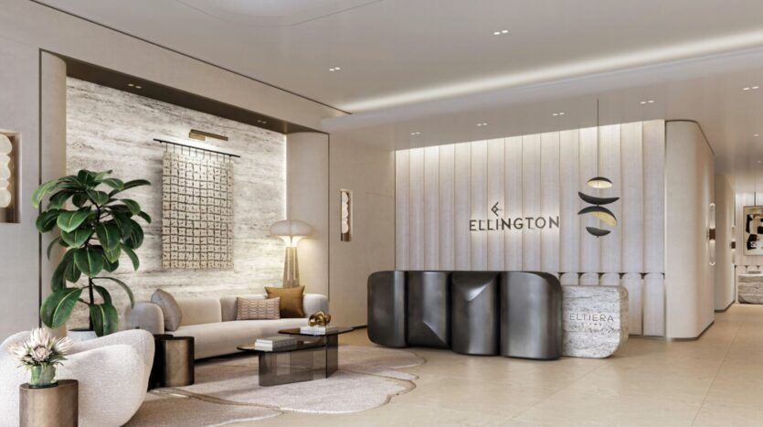 A modern and elegant reception area with neutral tones, contemporary furniture, wall art, indoor plants, and a black reception desk. The wall behind the desk displays the "Ellington" and Eltiera Views logos in elegant lettering.