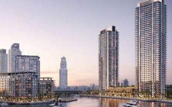 Des tours modernes et des appartements en bord de mer entourent le port de plaisance de Creek Bay, avec des yachts, des palmiers et une voie d'eau calme, sous un ciel doux en début de soirée.