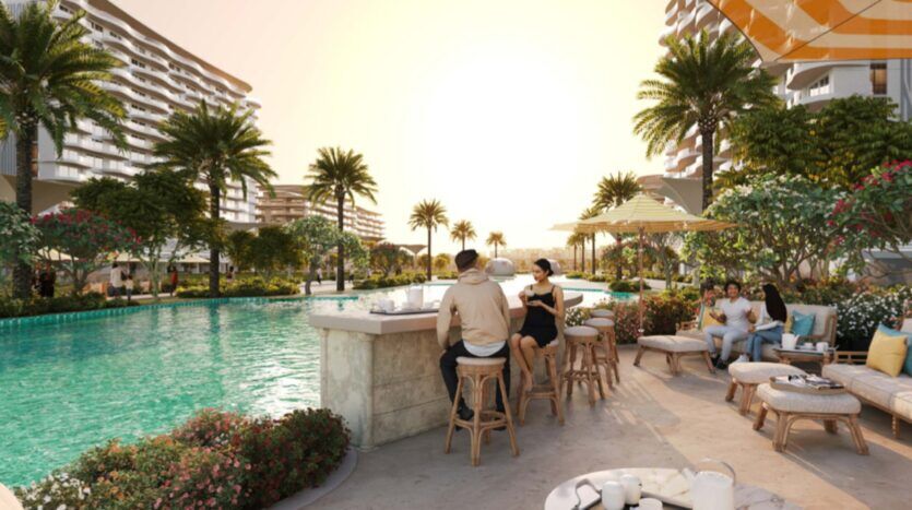 Al atardecer, la gente se sienta en el bar y en el salón de la piscina, rodeados de palmeras, flores y edificios modernos, creando un ambiente relajado de balneario tropical que recuerda la vibrante energía de la Piazza Roma.