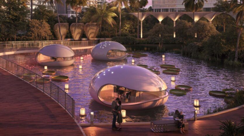 Tres estructuras futuristas con forma de góndola flotan en un estanque con grandes nenúfares cerca de la Piazza Roma, rodeadas de plantas tropicales y edificios modernos. Luces cálidas iluminan la escena mientras una pareja se encuentra en una terraza de madera junto al agua.