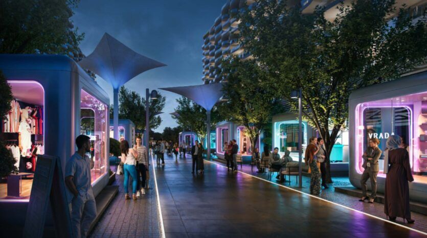 Una moderna calle peatonal al atardecer, con gente caminando y sentándose. Tiendas futuristas con fachadas de cristal e iluminación de colores bordean ambos lados, y árboles y marquesinas iluminadas decoran la animada escena de la Piazza Roma.