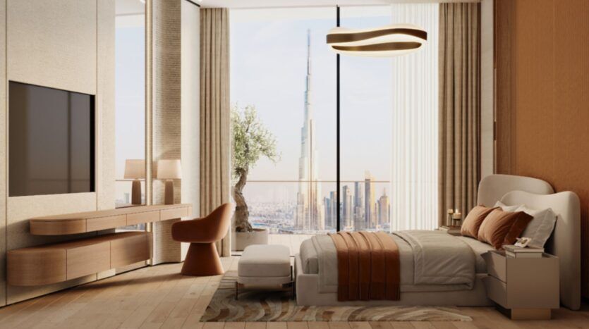 Chambre à coucher moderne avec un décor neutre et brun, un grand lit, une télévision, des meubles en bois, et des fenêtres allant du sol au plafond révélant un paysage urbain et le gratte-ciel Skyflame en arrière-plan.