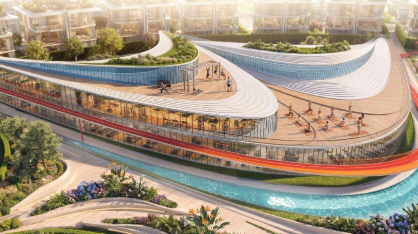 Le bâtiment de verre moderne et incurvé de Greenz by Danube comprend une salle de sport et de yoga sur le toit qui donne sur des jardins paysagers, une route sinueuse et une étroite piscine bleue ou un plan d'eau, avec des maisons contemporaines à l'arrière-plan.