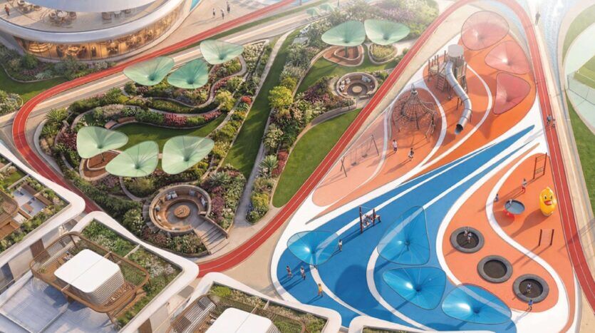 Vue aérienne d'une aire de jeux moderne à Greenz by Danube, avec des surfaces colorées bleues et orange, des structures d'escalade, des balançoires et des sièges ombragés à côté de jardins paysagers et de sentiers de promenade sinueux.