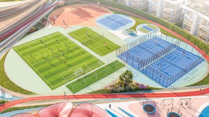 Vue aérienne de Greenz by Danube, montrant un complexe sportif coloré avec un terrain de football, des courts de tennis, des courts de paddle bleus, une piste de course et des personnes jouant activement ou faisant de l'exercice. Des bâtiments modernes entourent les courts.