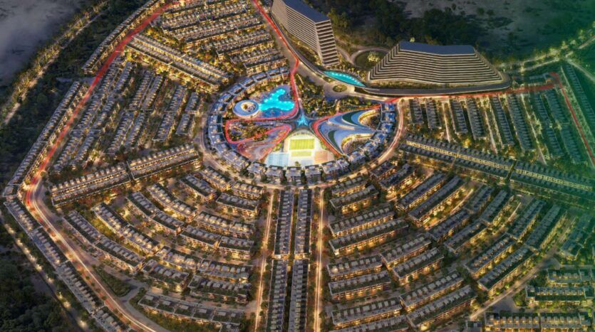 Vue aérienne de Greenz by Danube, un complexe résidentiel circulaire, très lumineux, avec des rangées de maisons rayonnant vers l'extérieur à partir d'une zone centrale animée avec des piscines, des allées colorées et deux grands bâtiments modernes à l'arrière-plan.