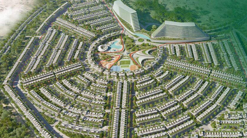Vue aérienne de Greenz by Danube, un complexe résidentiel moderne et circulaire dont les rangées de maisons rayonnent à partir d'une zone centrale comprenant des piscines, des espaces verts et deux grands bâtiments incurvés. La zone environnante est verdoyante et luxuriante.
