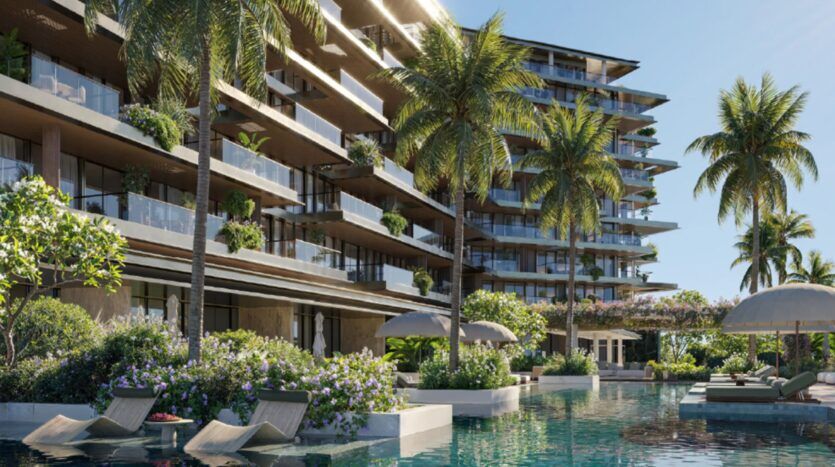 Le complexe moderne de luxe Cheval Residences est doté de nombreux balcons, de plantes luxuriantes et de palmiers. Une piscine d'un bleu limpide avec des chaises longues et des parasols se trouve au premier plan sous un ciel clair et ensoleillé.