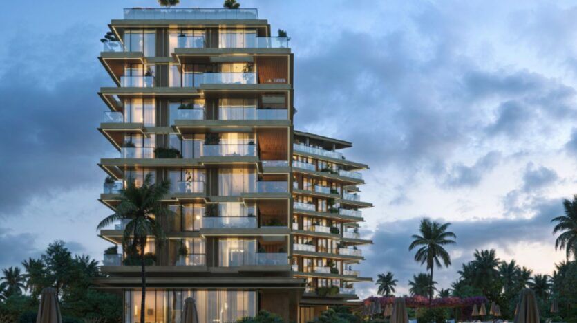 Un bâtiment moderne de plusieurs étages avec des balcons en verre, illuminés au crépuscule, entourés de palmiers et de verdure luxuriante sous un ciel nuageux - un cadre emblématique de Cheval Residences.