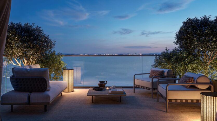 Le patio extérieur des résidences Cheval comprend des sièges rembourrés, une table basse et des arbres en pot qui donnent sur un plan d'eau calme au crépuscule, avec un éclairage doux qui crée une atmosphère relaxante.
