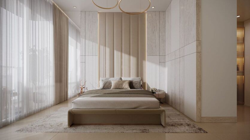 Une chambre à coucher moderne et minimaliste de Derby Heights avec un lit beige capitonné, une grande tête de lit rembourrée, une literie neutre et deux tables de nuit. Des rideaux transparents couvrent les hautes fenêtres, remplissant l'espace de lumière naturelle.