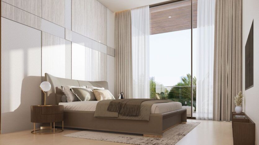 Chambre à coucher moderne à Derby Heights avec un grand lit, une literie neutre et une table de chevet ronde avec une lampe. Une fenêtre du sol au plafond avec des rideaux en voilage laisse entrer la lumière naturelle, révélant la verdure à l'extérieur. La télévision murale fait face au lit.
